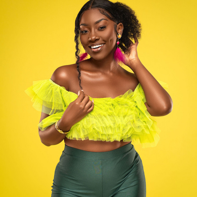 Reniece Bonnett smiling in a bright yellow ruffled top with pink feather earrings